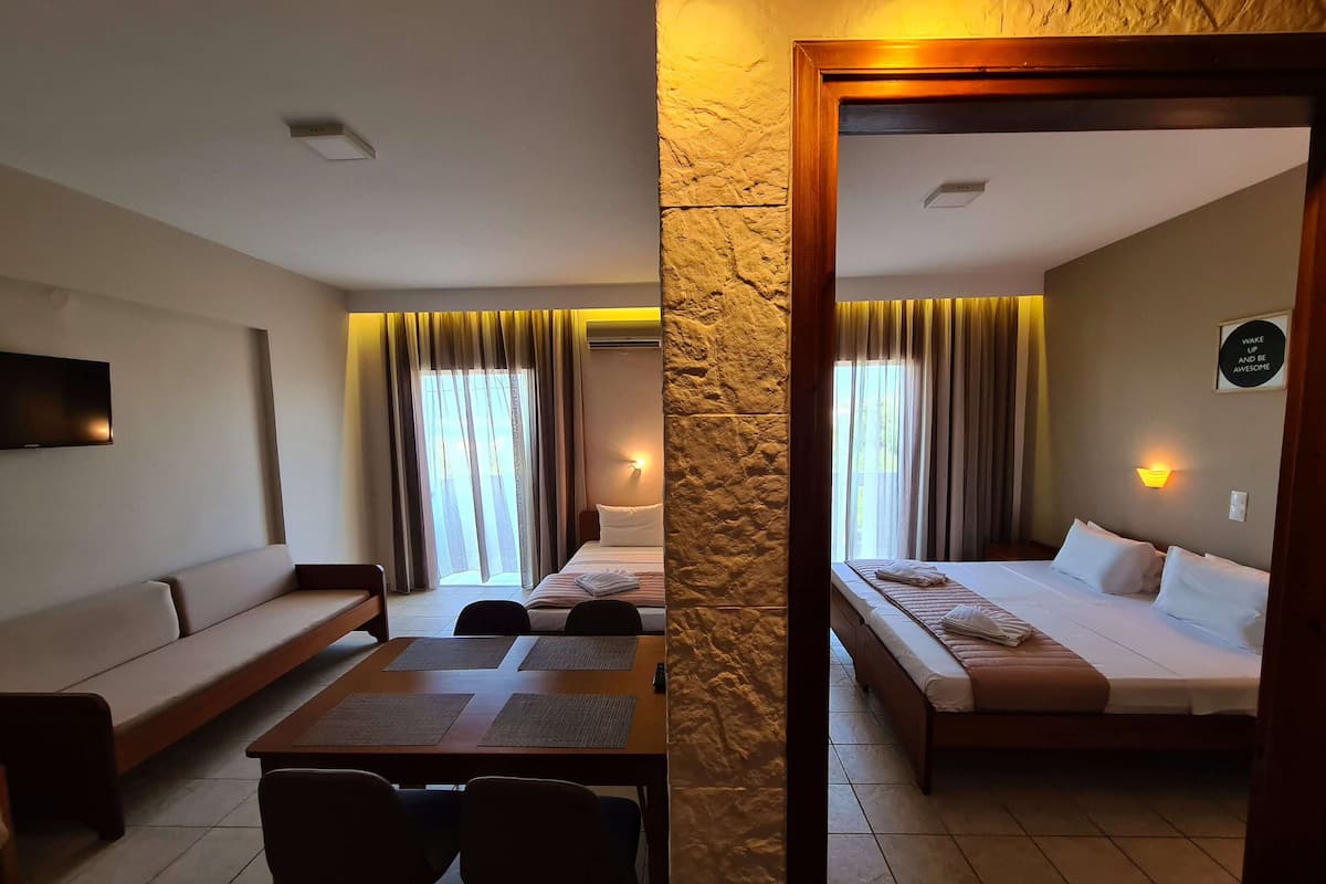 A hotel room with a sofa, a dining table with chairs, a bed, and a TV mounted on the wall.