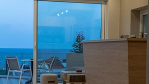 A modern interior with a large sliding glass door leading to a balcony overlooking the sea. - Abella Hotel (Chania)