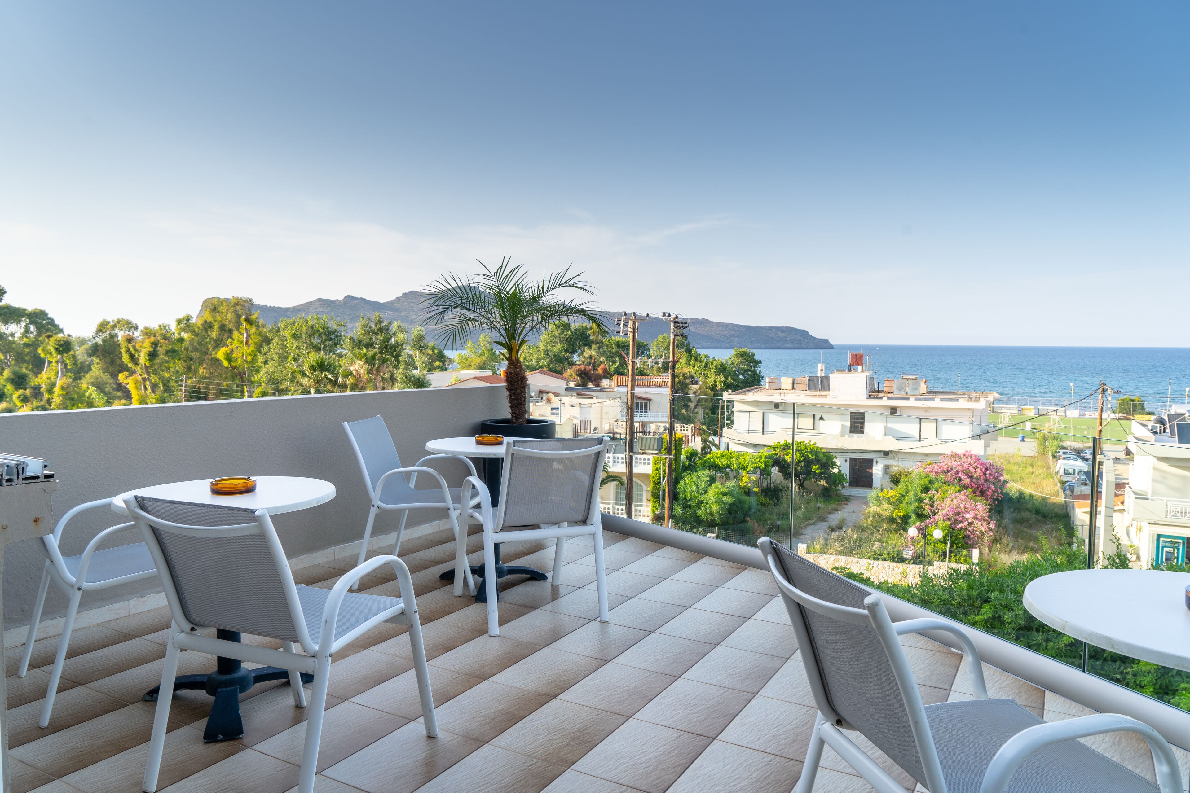 Eine Terrasse mit weißen Stühlen und Tischen mit Blick auf die Küste, mit Gebäuden und Grünflächen.