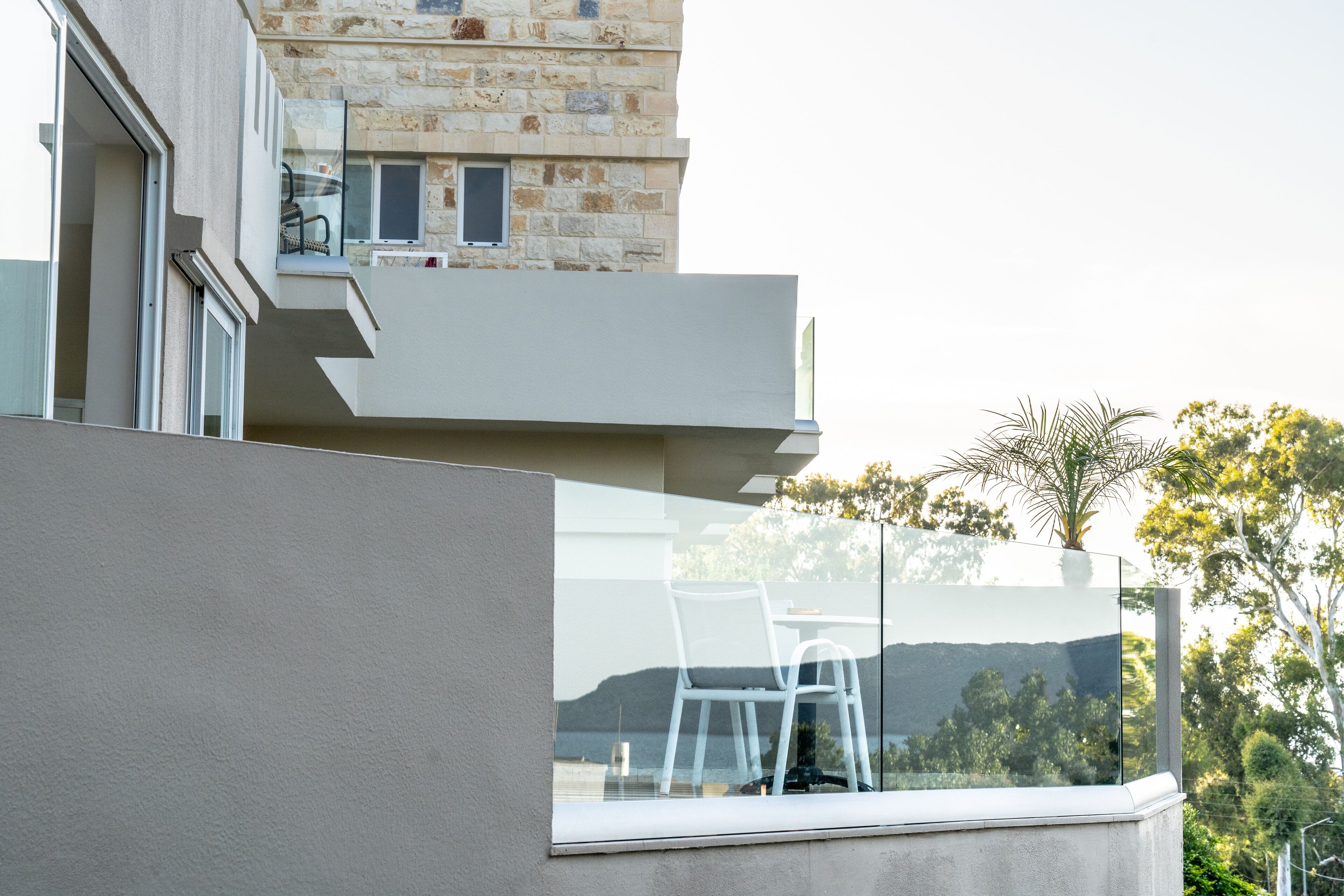 Un bâtiment moderne doté d’un balcon, d’une façade en pierre et offrant une vue sur les arbres et les collines.