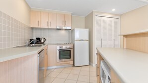 Une cuisine de taille réduite avec des meubles de couleur bois clair, une cuisinière en acier inoxydable, un réfrigérateur blanc et un dosseret carrelé.