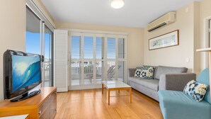 Un salon moderne avec un téléviseur à écran plat, un canapé gris, un fauteuil bleu et une table basse en bois.