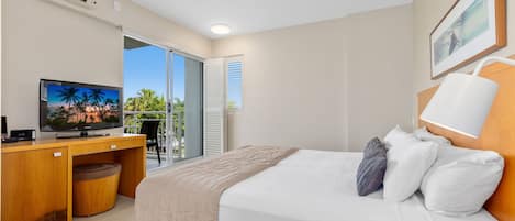 Une chambre d’hôtel avec un lit, un bureau avec une télévision, une fenêtre donnant sur un paysage agréable et un ventilateur de plafond.