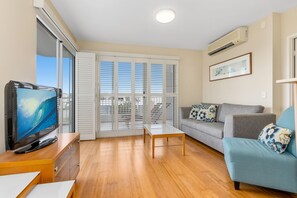 Relax in this stylish living room with a sofa, flat-screen TV, and sliding glass door leading to a balcony.
