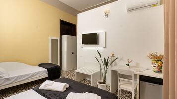 A hotel room with two beds, a desk, a chair, a small table, a potted plant, a television, and a minibar.