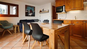 A compact kitchen with wooden cabinets, a microwave, and a dining area with a table and chairs. - 2-room cabin apartment in Les Houches, 4 pax (Les Houches)