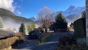 A mountain lodge with a stone bridge, a path leading to the entrance, and a view of snow-capped mountains. - 2-room cabin apartment in Les Houches, 4 pax (Les Houches)