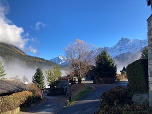 A mountain lodge with a stone bridge, a path leading to the entrance, and a view of snow-capped mountains.