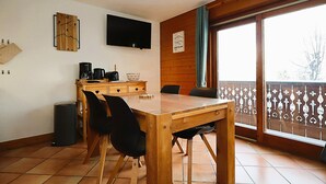 A dining area with a wooden table and chairs, a television mounted on the wall, and a window with a view of the outdoors. - 2-room cabin apartment in Les Houches, 4 pax (Les Houches)