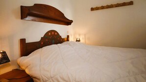 A neatly made bed with a wooden headboard, a bedside lamp, and a wall-mounted shelf. - 2-room cabin apartment in Les Houches, 4 pax (Les Houches)