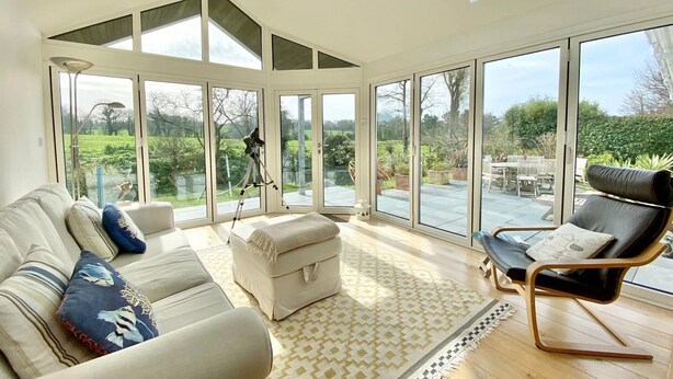 A spacious room with a large window, a telescope, a sofa, a chair, and a patterned rug.