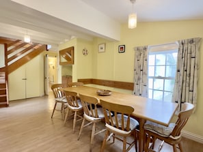 Ein Essbereich mit Holztisch und Stühlen, einer Treppe und einem Fenster mit Vorhängen.