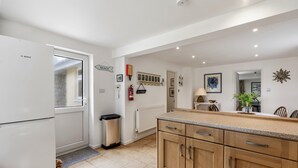 A kitchen with wooden cabinets, a Bosch refrigerator, a trash bin, a radiator, and a wall-mounted shelf. - Loughrigg -  a bungalow in the centre of Rock with parking (Rock)