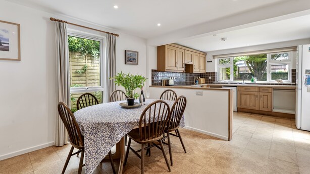 A modern kitchen with wooden cabinets, a dining area with a table and chairs, and a view of greenery outside. - Loughrigg -  a bungalow in the centre of Rock with parking (Rock)