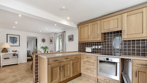 A modern kitchen with wooden cabinets, a built-in oven, and a countertop. - Loughrigg -  a bungalow in the centre of Rock with parking (Rock)