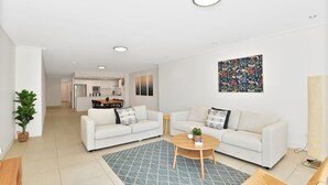 En moderne stue med to hvide sofaer, et sofabord og et køkken i baggrunden.