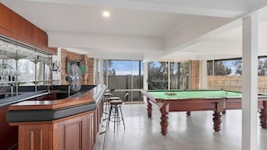 A pool table in a spacious room with a bar area and a fan.