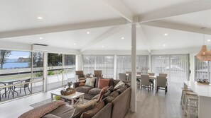 A spacious living area with a large window overlooking a body of water, a seating area with a sofa and chairs, and a dining area with a table and chairs.