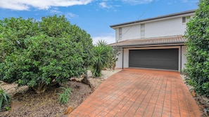 A residential property with a paved driveway leading to a garage, surrounded by lush greenery and a clear sky.