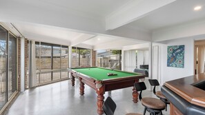A pool table in a spacious room with large windows, a bar area, and a painting on the wall. - Sunset Lake House - Pool, Lake Views & Beach (The Entrance North)