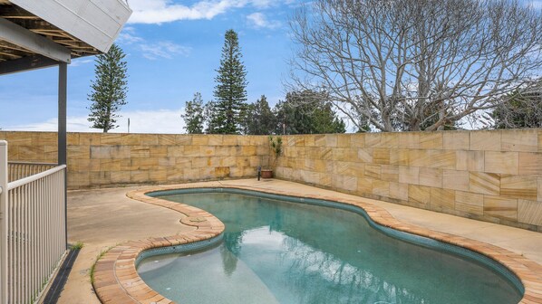 A swimming pool with a curved edge, surrounded by a stone wall and a metal fence.