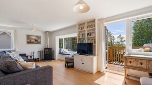 A spacious living room with a sofa, a bookshelf, a television, and a view of the outdoors through large windows. - Pen-Wethers -  Holiday Home that sleeps 8 guests  in 4 bedrooms (Rock)