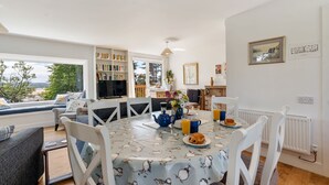 A dining area with a table set for two, a bookshelf, and a television in the background. - Pen-Wethers -  Holiday Home that sleeps 8 guests  in 4 bedrooms (Rock)