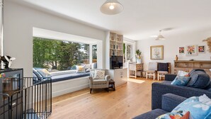 A modern living room with a large window, a sofa, a dining table, and a bookshelf. - Pen-Wethers -  Holiday Home that sleeps 8 guests  in 4 bedrooms (Rock)