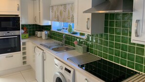 A modern kitchen with white cabinets, a stainless steel range hood, a built-in washing machine, and a green tiled backsplash. - Newly Refurbished, old Bull Pen cottage near Lewes East Sussex (Barcombe)