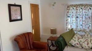 A living room with a brown leather armchair, a wooden door, a lamp, and a sofa with patterned cushions. - Newly Refurbished, old Bull Pen cottage near Lewes East Sussex (Barcombe)