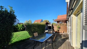 Una terraza de madera con una mesa y sillas, rodeada de un césped cuidado y una valla de madera.