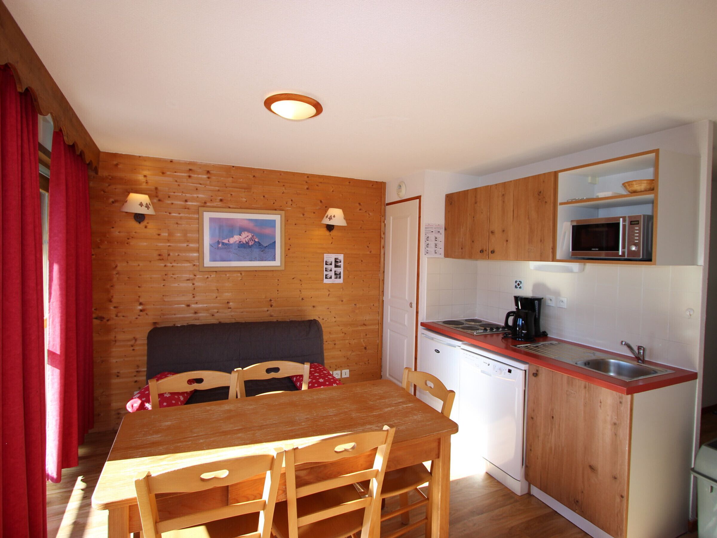 A compact kitchen with wooden cabinets, a microwave, a dishwasher, and a dining area with a table and chairs.