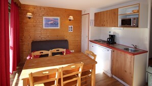 Een compacte keuken met houten kastjes, een magnetron, een vaatwasser en een eethoek met een tafel en stoelen.