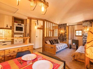 A cozy room with a bed, a dining table set for two, a kitchen area with a stove and oven, and a stone wall.