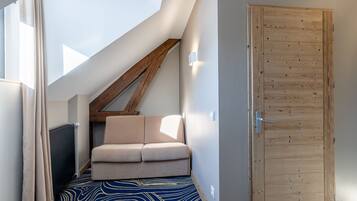 A narrow hallway with a sloped ceiling, a wooden door, and a beige chair.