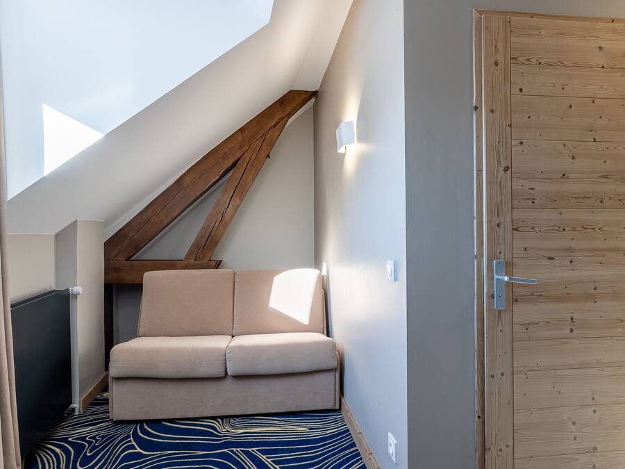 A narrow hallway with a sloped ceiling, a wooden door, and a beige chair.