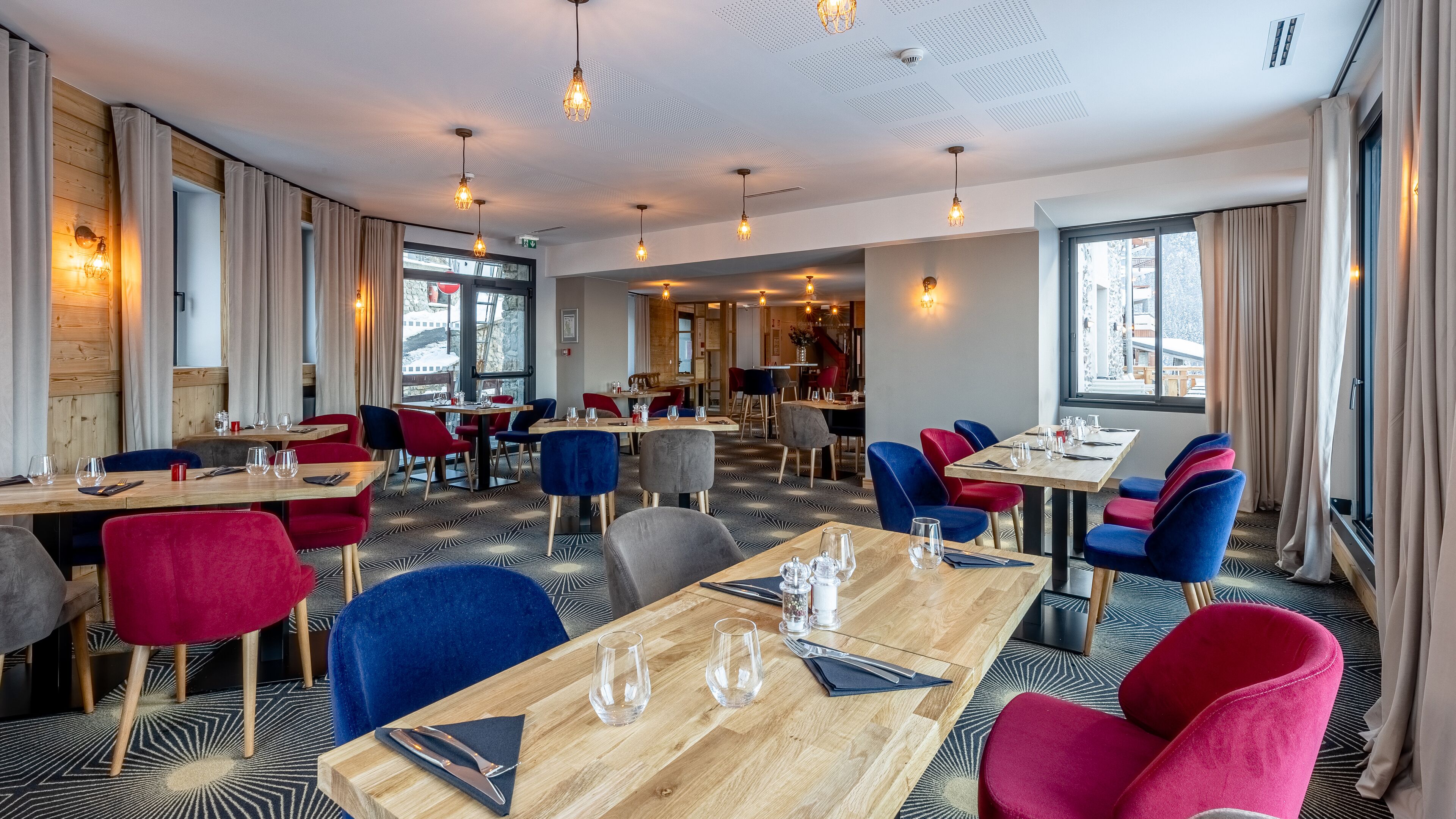 Ein Restaurant mit mehreren Tischen und Stühlen, Holzboden und großen Fenstern.