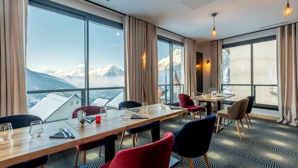 A dining area with a view of snow-capped mountains, large windows, and modern furnishings. - Madame Vacances Hôtel les Cimes (Vaujany)
