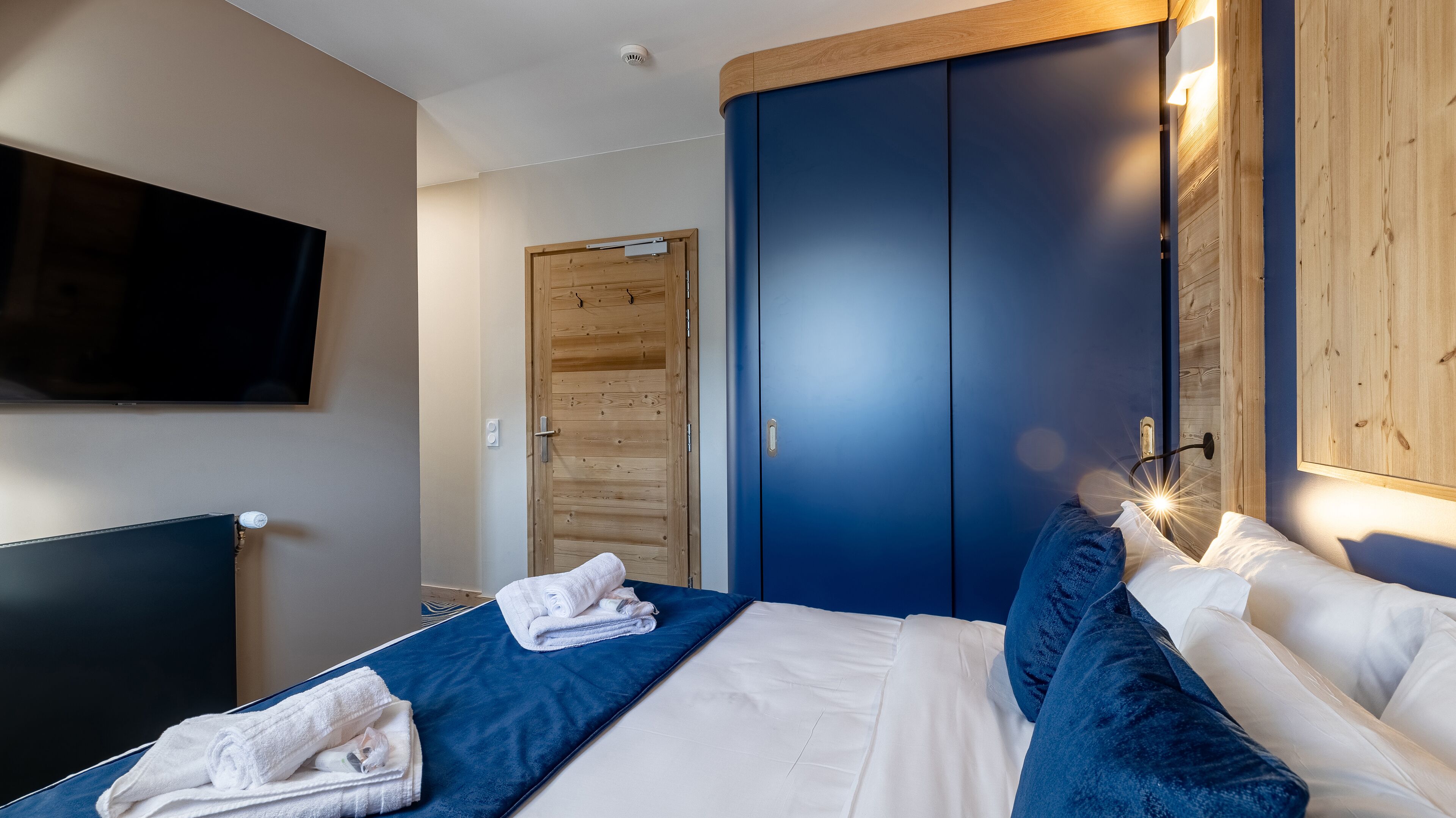 A hotel room with a bed, a TV, a wardrobe, and a wooden door.