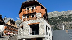 A multi-story hotel with a stone facade and wooden balconies, featuring a mountain view. - Madame Vacances Hôtel les Cimes (Vaujany)