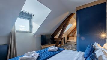 A bedroom with a skylight, a bed with blue bedding, a wooden ceiling, and a view of the sky.