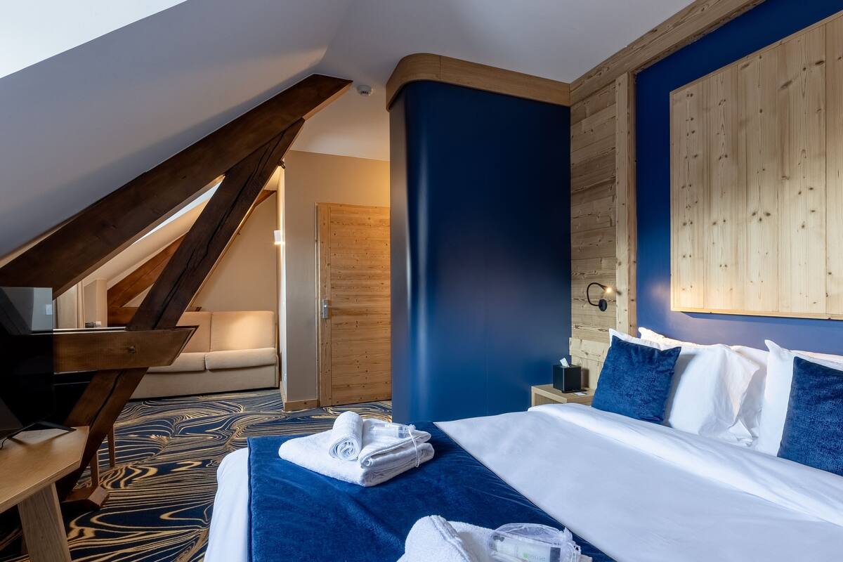 Ein Hotelzimmer mit Bett, Holz-Kopfteil, blauer Akzentwand, einer Holztreppe und einem Nachttisch mit Lampe.