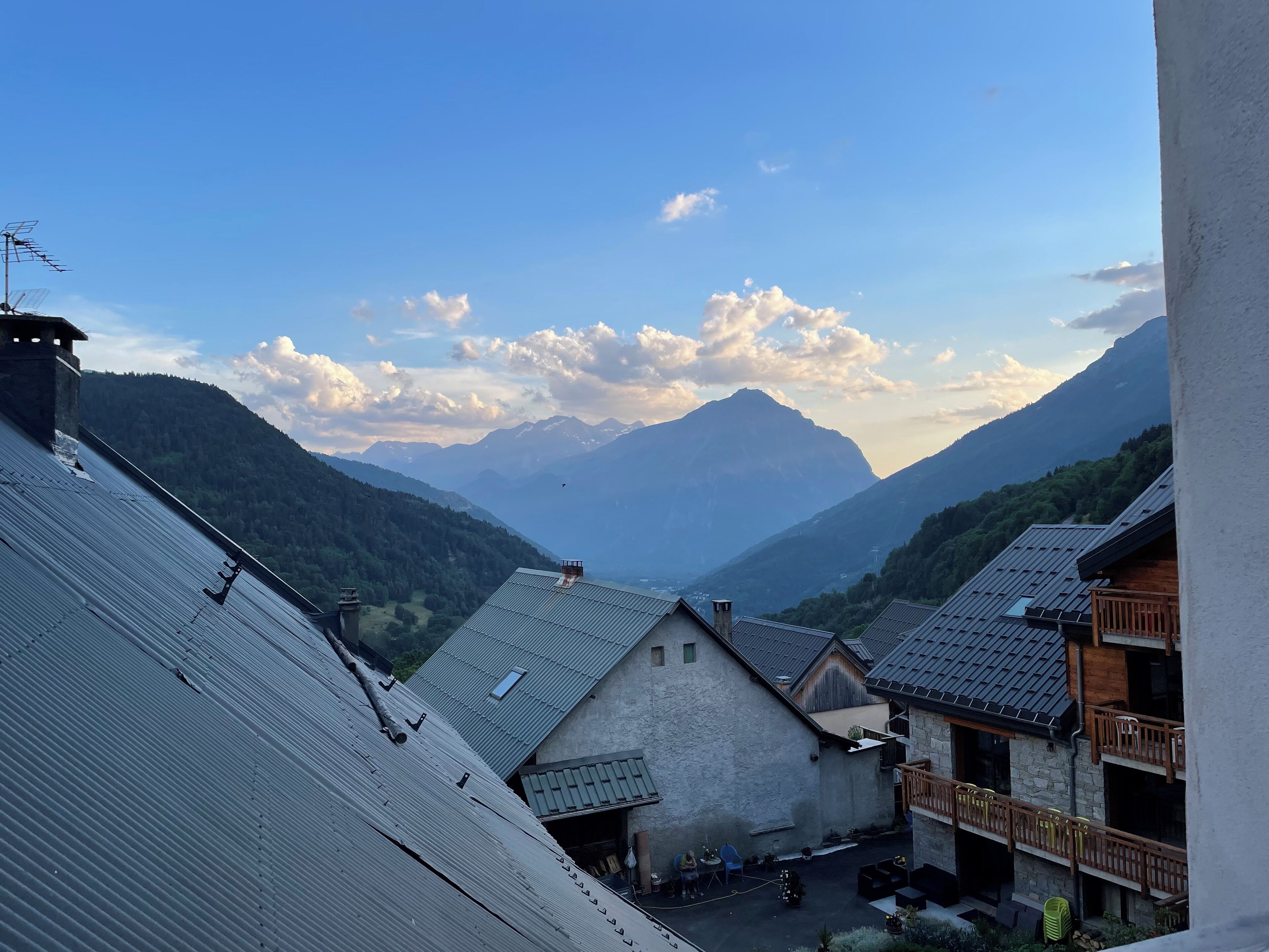 A mountain village with traditional buildings, a paved courtyard, and a view of distant mountains.