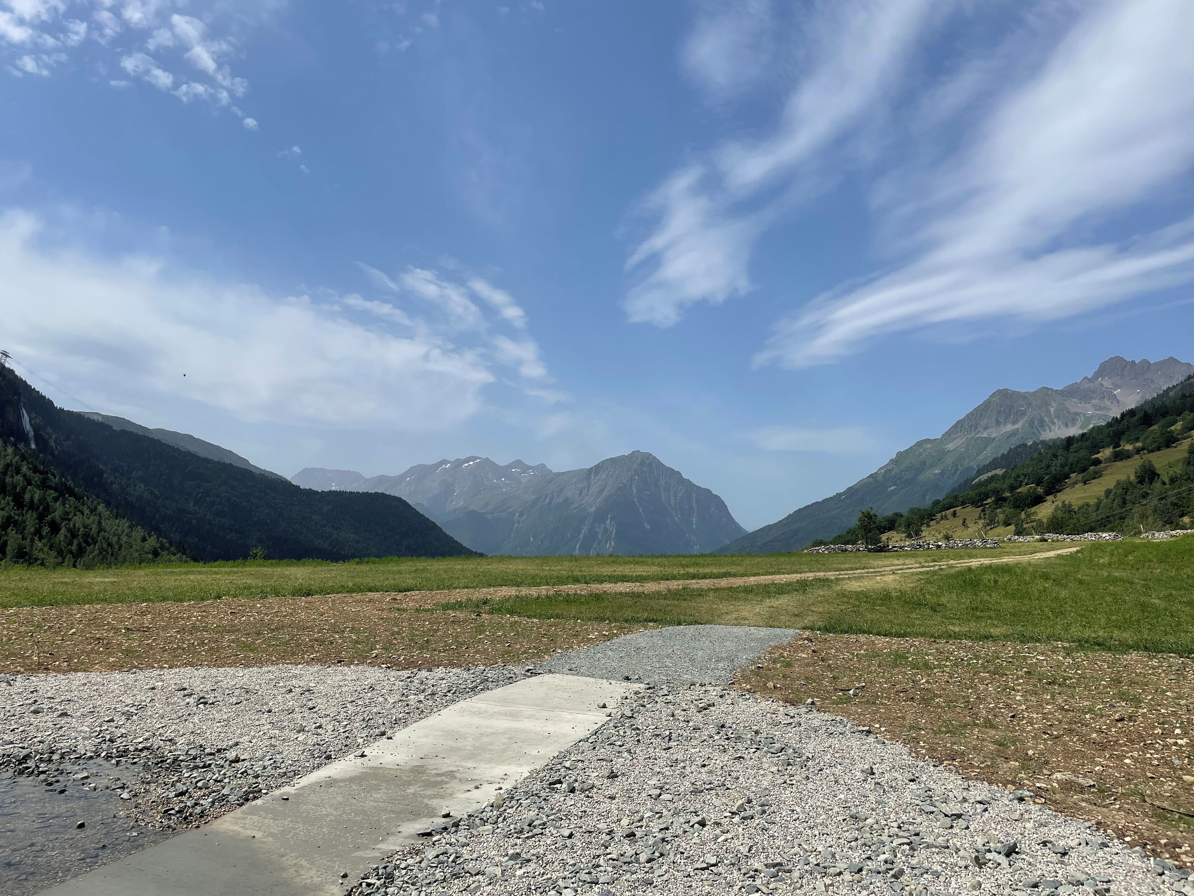 A mountainous landscape with a clear sky and a gravel path leading through a green field.
