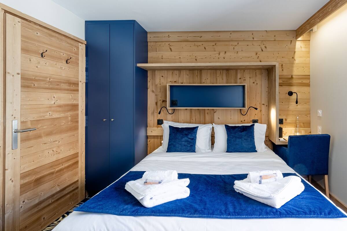 Ein Hotelzimmer mit einem Bett, einem Holzschrank, einem an der Wand befestigten Fernseher und einem Schreibtisch mit Stuhl.