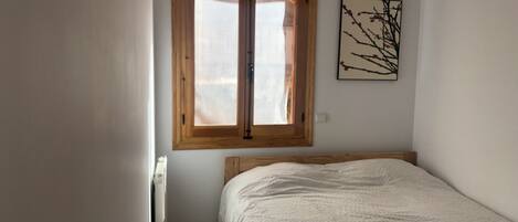 Ein Schlafzimmer mit einem hölzernen Bett, einem Fenster mit Holzrahmen und einem an der Wand befestigten Kunstwerk.