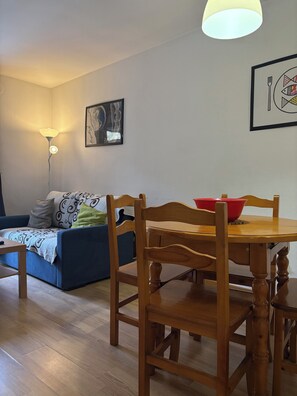 Un salon avec une table à manger en bois, un canapé bleu, une lampe sur pied et un tableau encadré au mur.