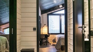Corredor estreito que dá para um quarto com cama, escrivaninha e cadeira.