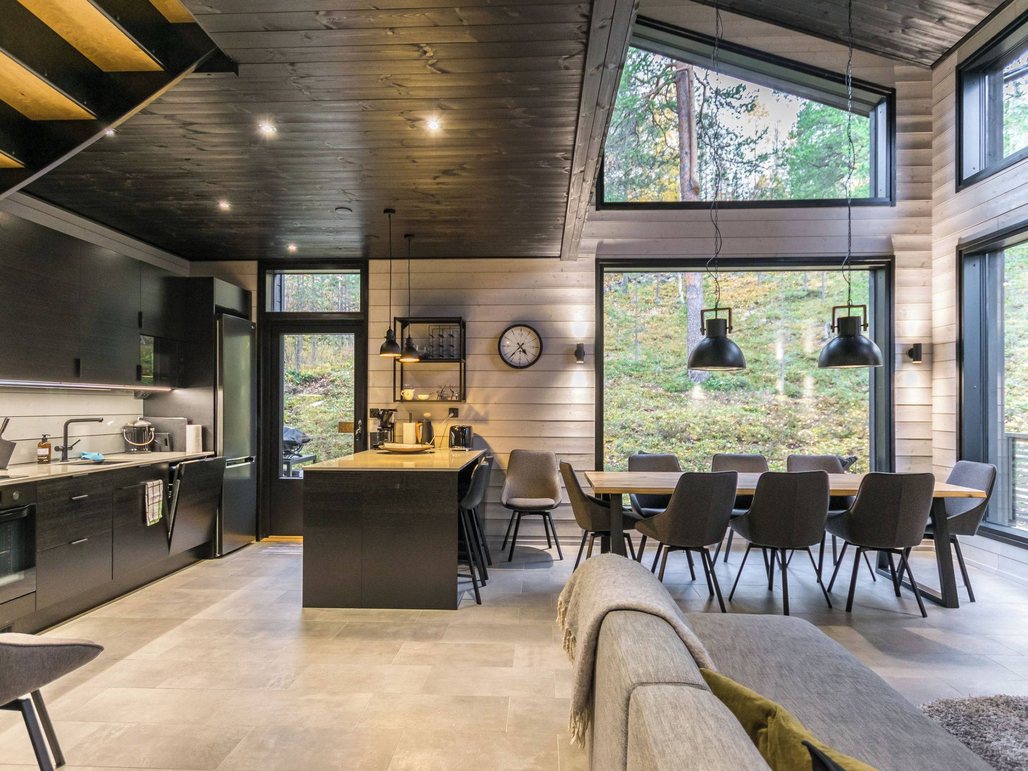 Cocina moderna con una isla central, comedor con sillas y grandes ventanales con vistas al exterior.