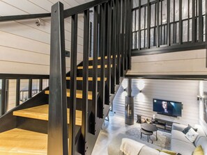 Un interior moderno con una escalera, una sala de estar con sofá y televisor, y una chimenea.